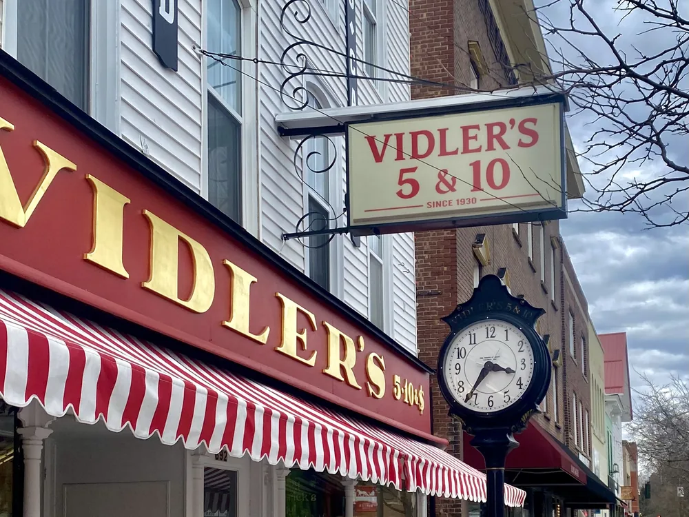 A small-business storefront with a street clock on a town main street